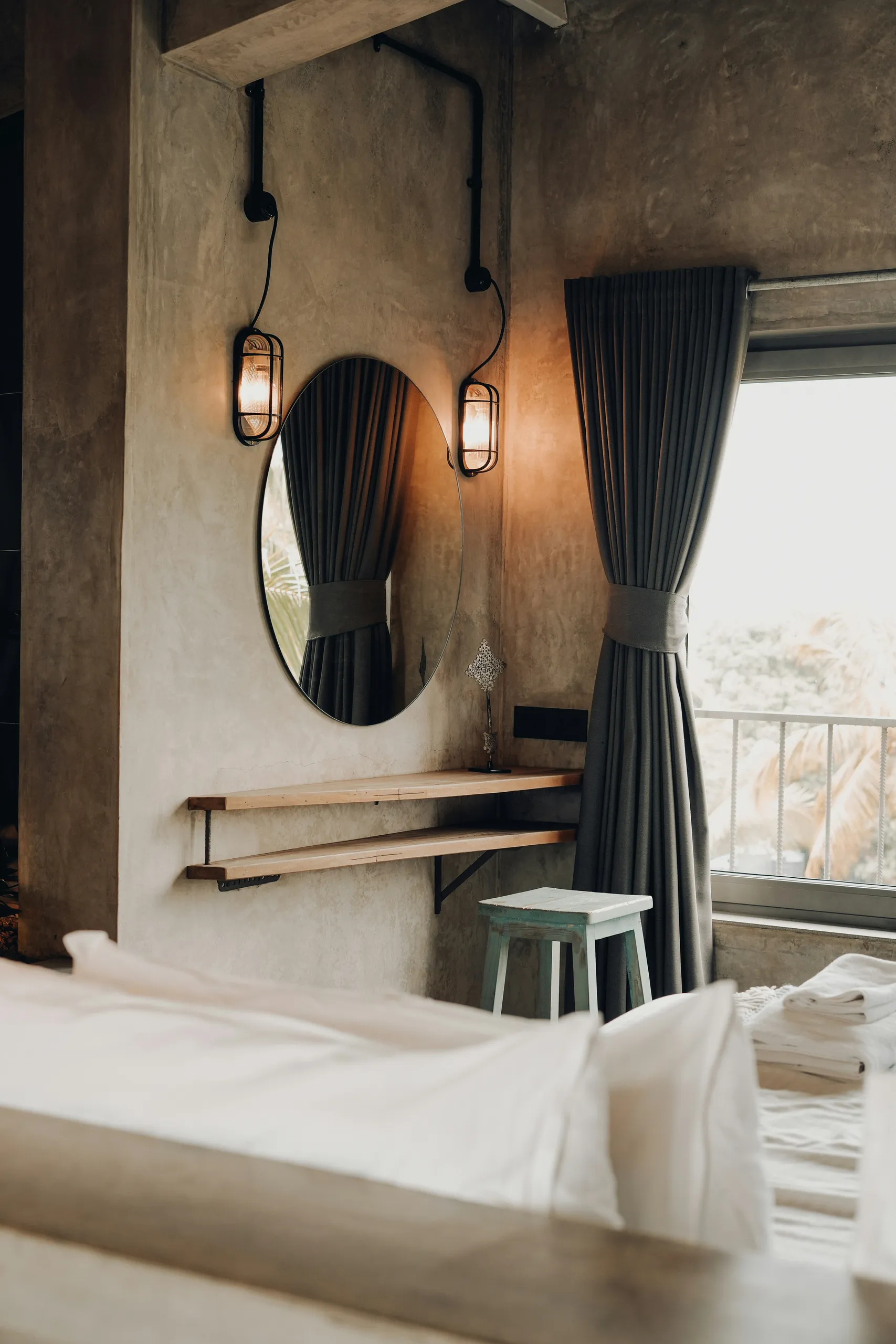 Espejo redondo sobre una estantería de madera, cortinas verde oscuro y un balcón con vistas — una habitación acogedora.