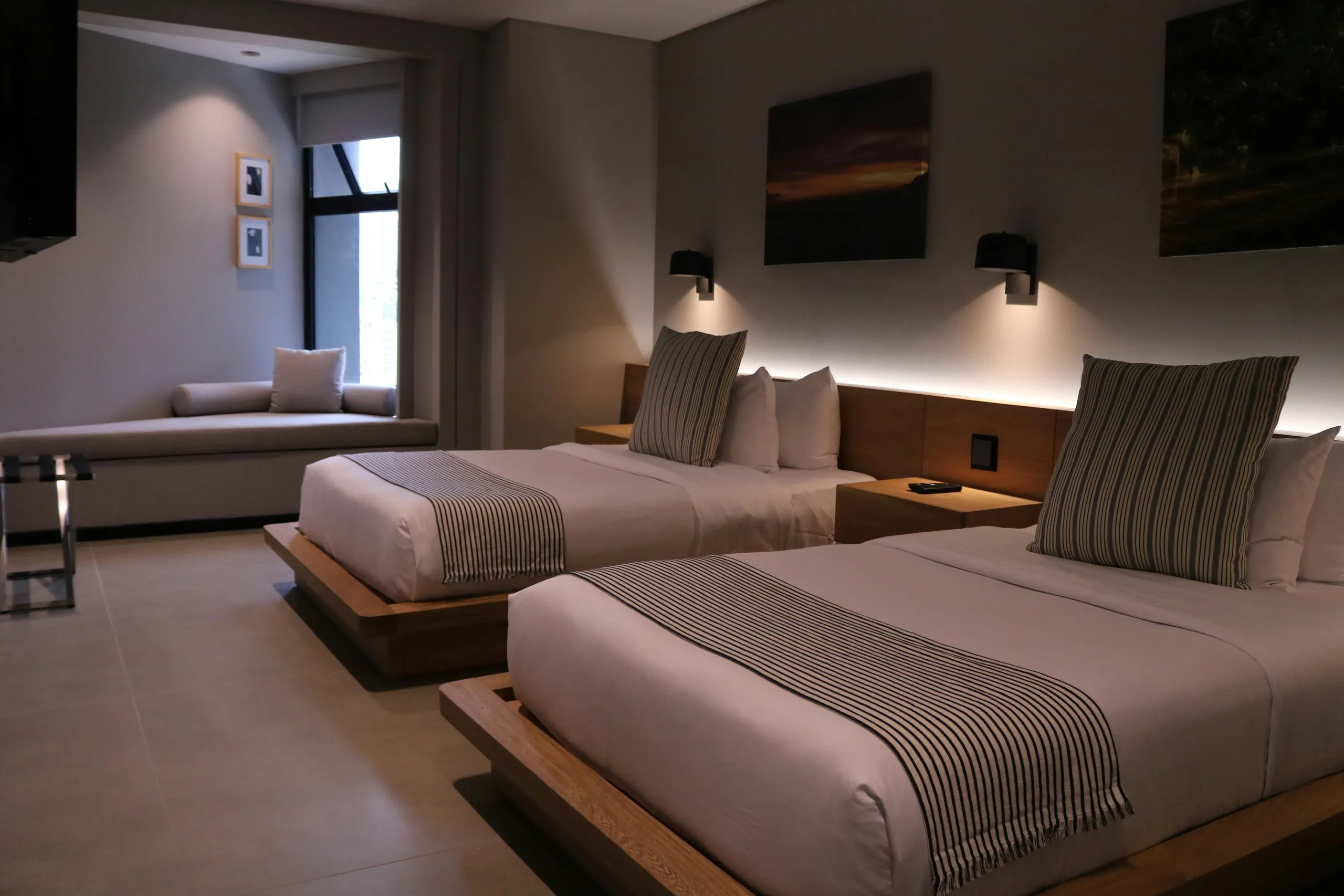 Habitación acogedora con dos camas, cabeceros de madera y la cálida luz de los apliques.