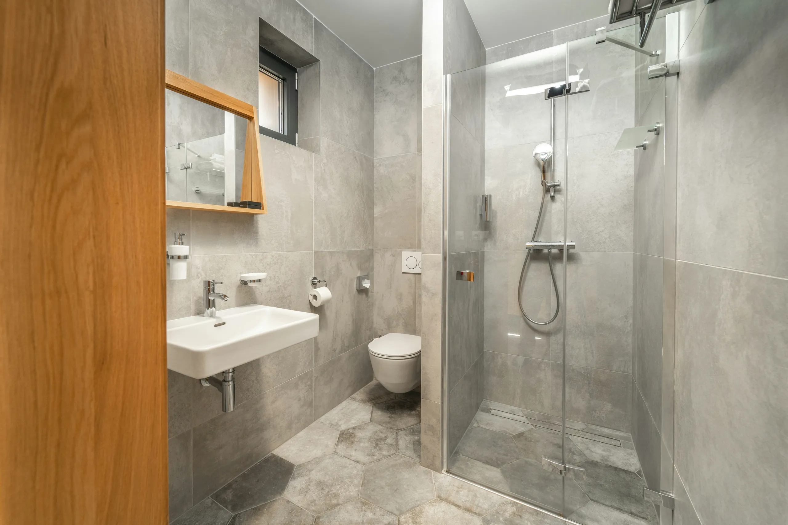 Baño con cabina de ducha, lavabo blanco y azulejos grises.